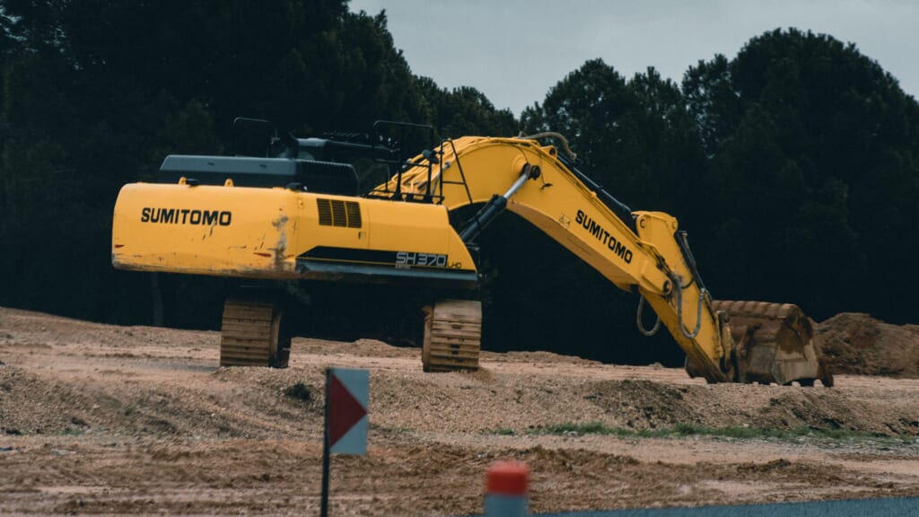 Yellow Sumitomo excavator working at a construction site near the road on a cloudy day.
