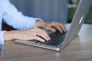 空き家管理サービス Crop faceless female entrepreneur wearing casual clothes sitting at wooden desk and browsing portable netbook in daylight