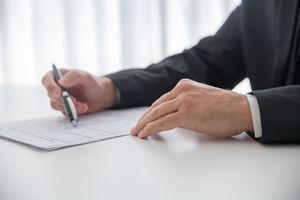 お墓の管理サービス Businessman signing important documents at office desk.